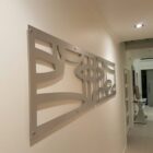 A modern hallway features a decorative metal wall art piece and a side table with an object.