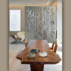 A wooden dining table with decorative bowls, a partition featuring weeping willow designs, and a modern chair.