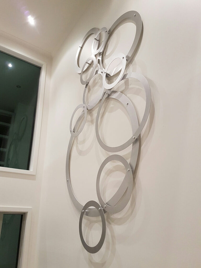 Metal wall sculpture featuring overlapping circular shapes on a light-colored wall.