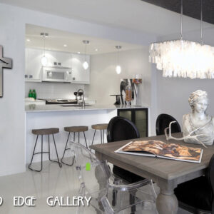 A modern kitchen-dining area with a breakfast bar, stools, and a contemporary chandelier. A bust and an open book are on the dining table. The wall features a cross and the text "COLD EDGE GALLERY.