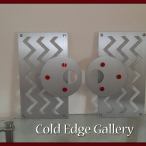 Two abstract metal art pieces with zigzag patterns and circular discs featuring red accents. Below, text reads "Cold Edge Gallery.