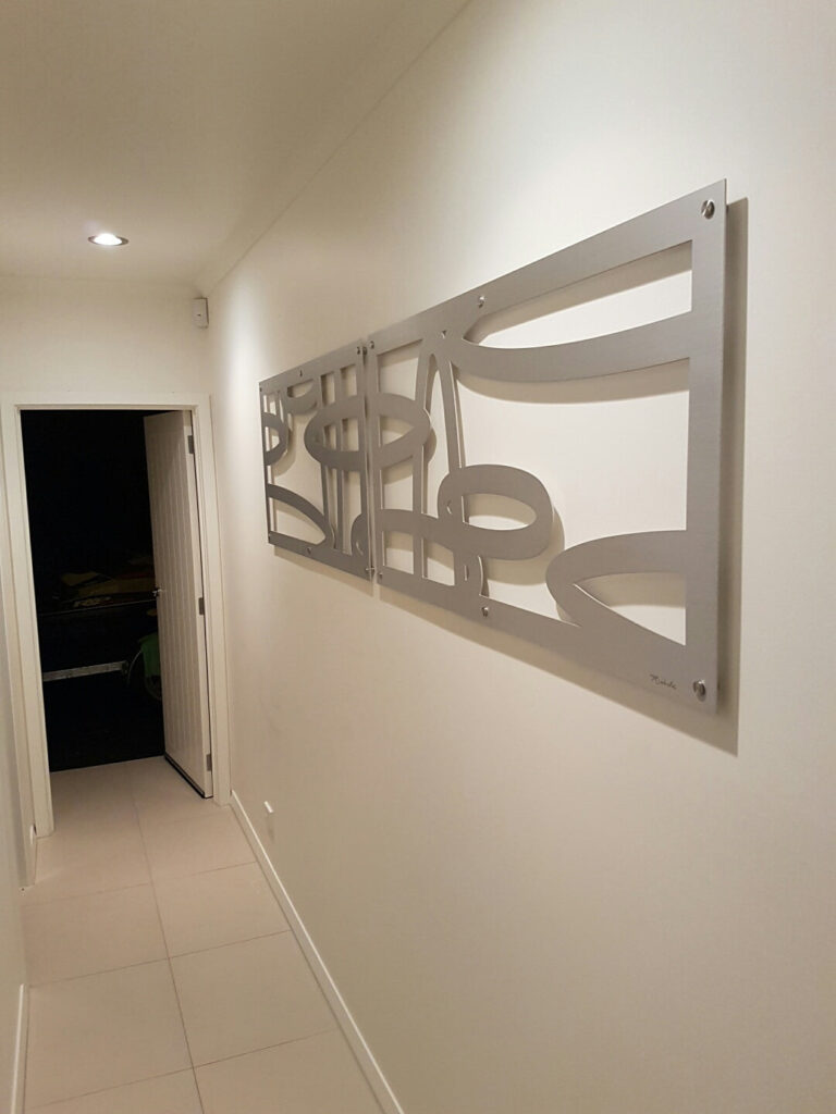 A modern hallway features a decorative metal wall art piece and a doorway leading to a darkened room.