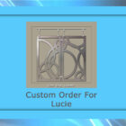 A framed image with text "Custom Order For Lucie" at the bottom and a decorative metal piece with abstract circular patterns in the center.