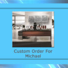 An office setting with a modern wooden desk and a chair behind it. The words "COLD EGE GALLERY" and "Custom Order For Michael" are displayed over the image, highlighting a custom piece of metal artwork.