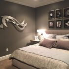 A sleek, modern metal wall sculpture with curved, wave-like shapes decorates a dark gray bedroom wall.