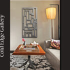 A modern living room with abstract wall art above a custom wooden table. The table holds a tray with a flower and book. A metal lamp hangs near a gray sofa and a patterned cushion. Text reads "Cold Edge Gallery.