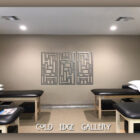 A room with two massage tables, each with a pillow. A geometrical metal wall art is centred on the back wall. The words "Cold Edge Gallery" are written at the bottom of the image.