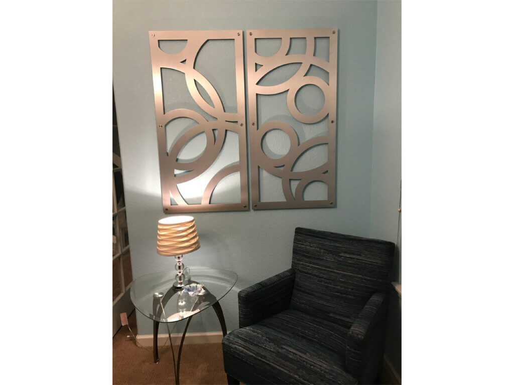 Two decorative wall panels hang above a glass side table with a lamp and a striped armchair.