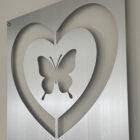 A metallic wall decoration featuring a cut-out design of a heart with a butterfly in the center.