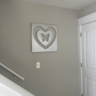 Wall art featuring a butterfly within a heart shape, mounted on a gray wall in a hallway near a white door and staircase.