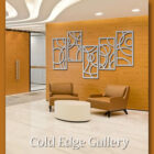 A minimalist gallery lobby featuring two brown chairs, a white round table, and abstract wall art on a wooden panel. A glass door and ceiling lights are in the background. Text reads "Cold Edge Gallery.