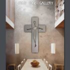 A minimalist metal wall sculpture in the shape of a cross is displayed above a dining table in a modern setting. Text at the top reads "Cold Edge Gallery.