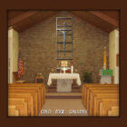 Interior of a chapel with wooden pews facing an altar. A crucifix is mounted on a brick wall behind the altar, which is draped in a white cloth. American and yellow flags are displayed on the left.