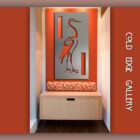 Wall-mounted artwork of a crane in Cold Edge Gallery. The artwork features cutouts and is displayed above a wooden cabinet with red patterned cushioning below it. The background is painted red and white.