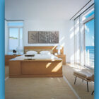 A modern bedroom featuring a light wood bed, matching furniture, and a triptych of tree-like metal artwork above the bed. The room has large windows with a view of the ocean. Text reads: "Cold Edge Gallery.
