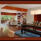 A modern open-plan living and dining area with wooden floors and large windows. A decorative room divider separates the spaces. The dining table has flowers, and there's a couch and chairs in the living area.