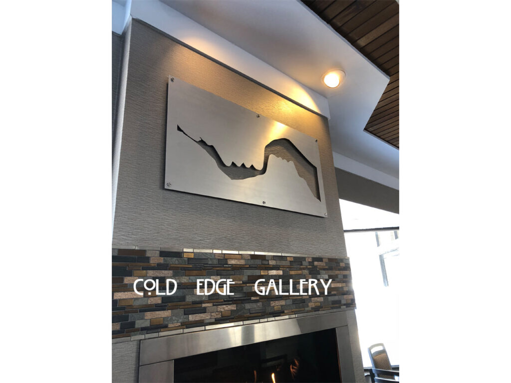 Metal wall art depicting a mountain range above a stone fireplace, with "COLD EDGE GALLERY" displayed below.