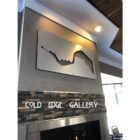 Metal wall art depicting a mountain range above a stone fireplace, with "COLD EDGE GALLERY" displayed below.