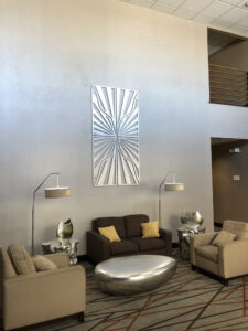 Modern lounge area with brown sofas, silver tables, and decorative wall art. Soft lighting from floor lamps.