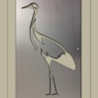 A custom metal wall art piece depicting a crane, created with intricate cut-out techniques. The artwork is elegantly displayed within a frame on a beige background with "Cold Edge Gallery" text at the bottom.