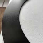 Close-up image of a black, circular metal object on a white surface, with visible textures and a small hole near the edge.