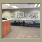 Reception area with a wooden desk, patterned seating, and metal wall art featuring human-like figures in various poses. Text in the bottom right corner reads "Cold Edge Gallery.