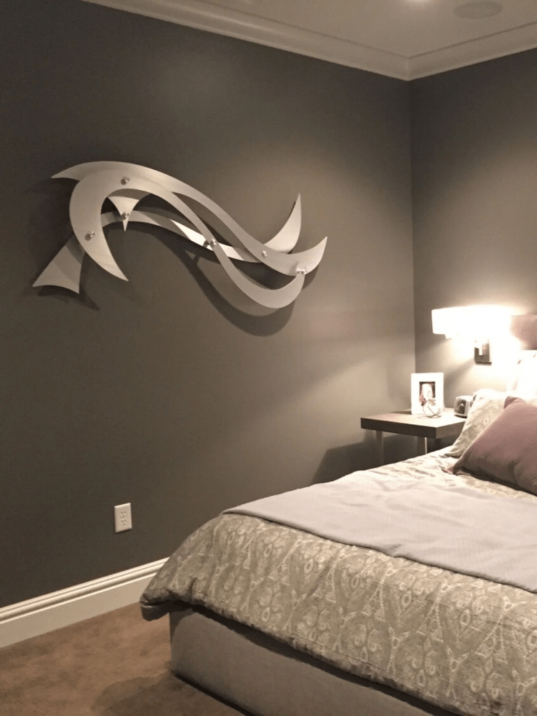 A modern bedroom features a bed with patterned bedding, a nightstand, and abstract wall art.