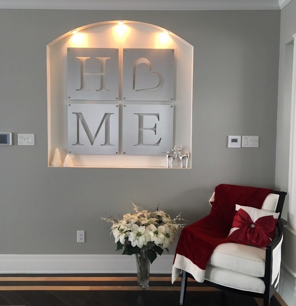 Brushed aluminum wall art spells "HOME" with a heart, beside a chair and floral arrangement.