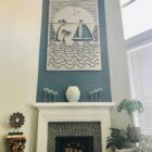 Metal wall art features a sunset scene with a sailboat, palm trees, and waves, above a decorative fireplace.