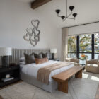 Modern bedroom featuring a bed with decorative pillows, a wooden bench, and large windows overlooking nature.
