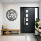 A modern entryway features a decorative Medusa wall art, a black door, and a wooden bench with cushions.