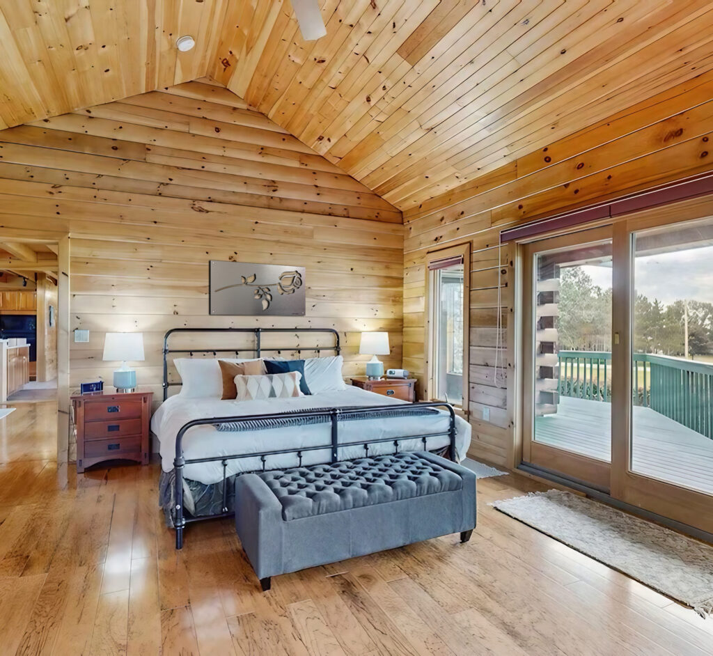 Cozy bedroom with wooden walls, a bed, nightstands, and sliding doors to a deck.