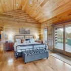 Cozy bedroom with wooden walls, a bed, nightstands, and sliding doors to a deck.