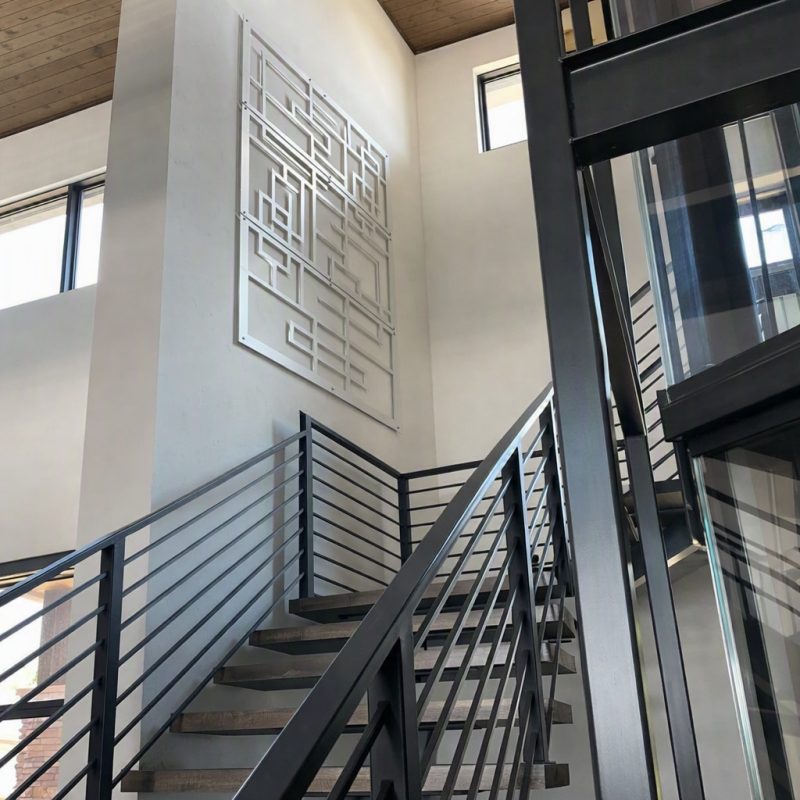 Staircase with metal railing, modern art installation on wall, large windows allowing natural light.