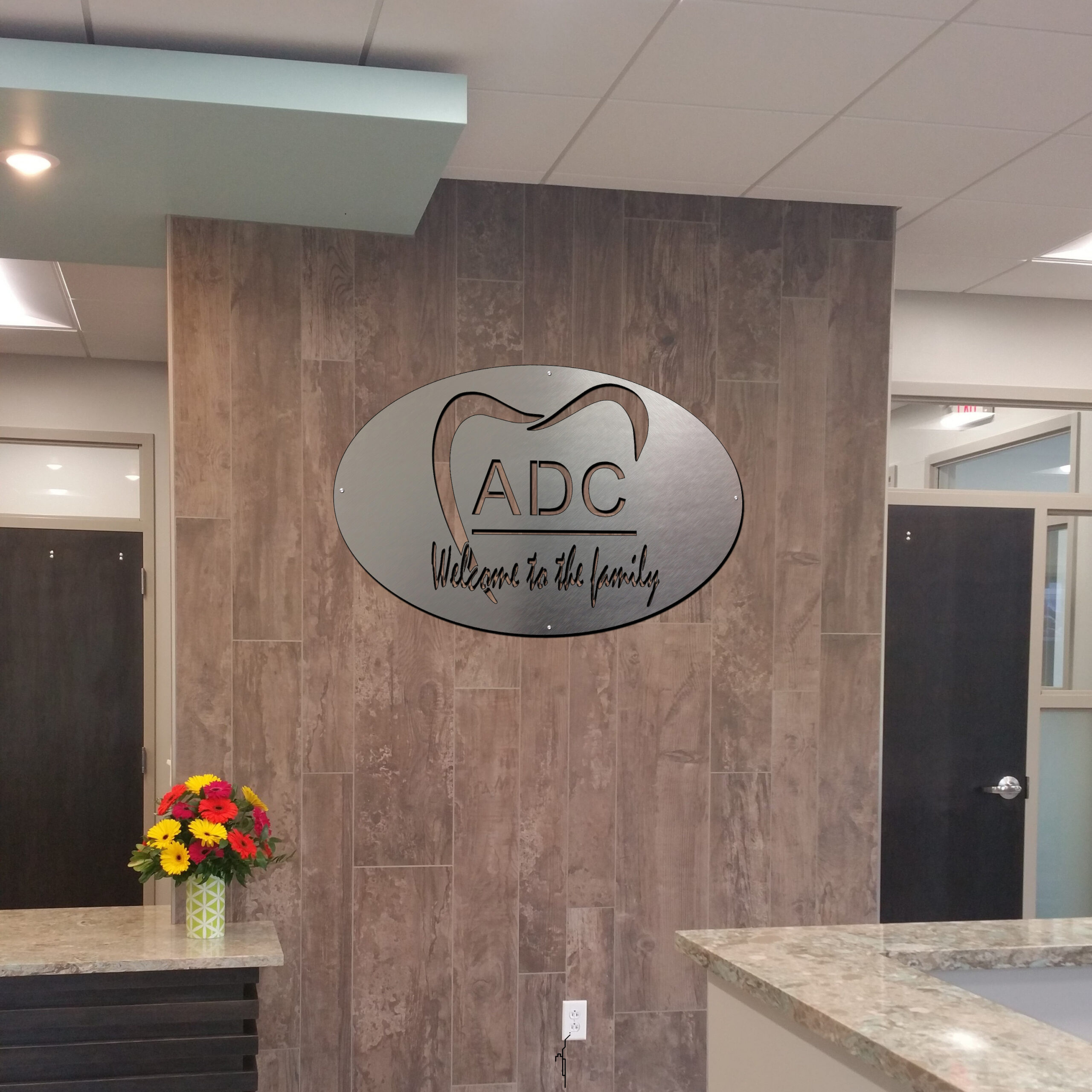 Signage on wall reads "ADC Welcome to the family," with a flower arrangement on the reception desk.