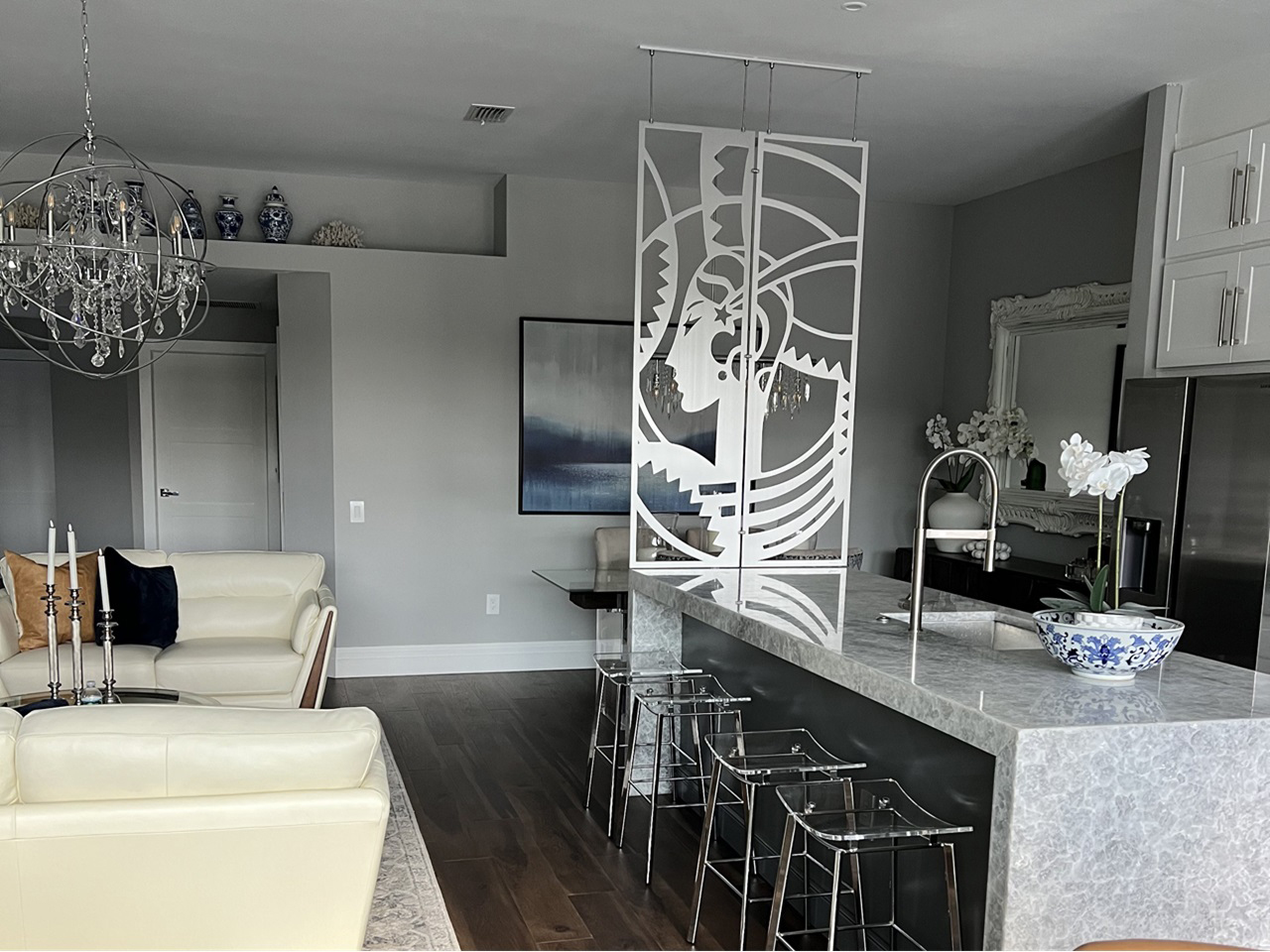 Modern kitchen and living area featuring a decorative partition, chandelier, and stylish furniture.
