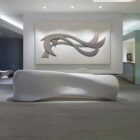 Modern office interior features a sleek white bench and abstract wall art, with large windows showcasing a sunset view.