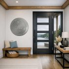 Circular metal wall art hangs beside a modern door, with a wooden bench and a table featuring decorative items.
