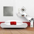 Metal wall art featuring a circular maze design hangs above a modern white sofa with red cushions and geometric shelves.