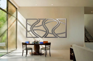 Modern dining area features a round table, chairs, and an abstract metal wall art piece. Natural light floods the space.