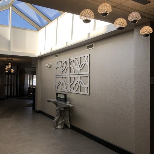 Bright hallway with decorative wall art, unique table, and hanging light fixtures. Natural light streams through skylights.
