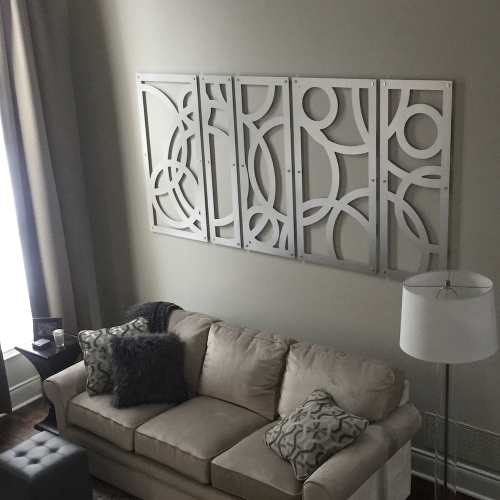 A cozy living room features a beige sofa with decorative pillows, a gray ottoman, and abstract wall art.
