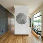A circular maze artwork is mounted on a white wall in a modern hallway with wooden flooring.