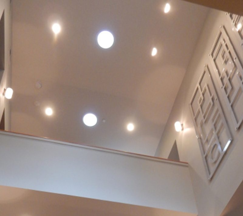 View of a modern interior with a high ceiling, recessed lights, and decorative wall panels.
