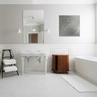 Bright bathroom features a freestanding sink, wooden cabinet, towels on a rack, and a decorative wall panel.